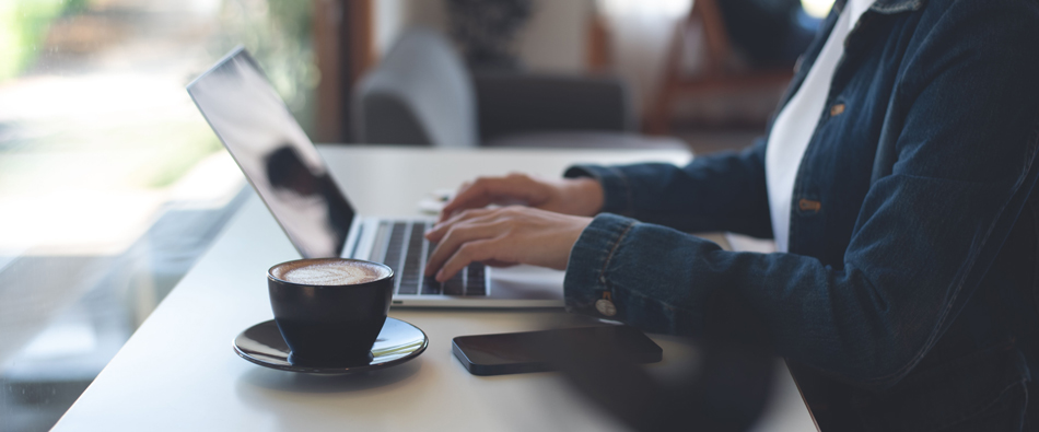 Person typing on a laptop at a cafe table, with a cup of coffee and a smartphone nearby.